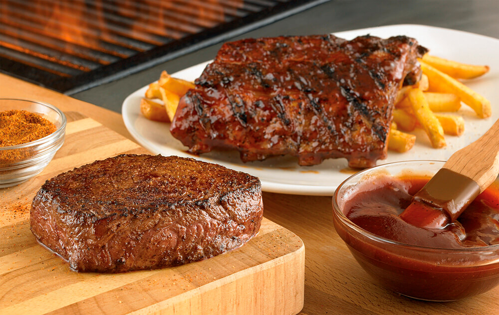 Prato branco com costela e batata, outras carnes na mesa com molho - Jackaroo Ribs n Steak.