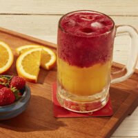 Caneca com Suco LaraMora, com fatias de laranja e morangos ao lado