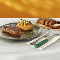 Steak The Outback Special servido com Jacket Potato como acompanhamento. Ao fundo, pão australiano cortesia.
