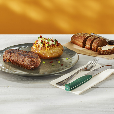 Steak The Outback Special servido com Jacket Potato como acompanhamento. Ao fundo, pão australiano cortesia.