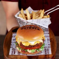 Atendente com uniforme vermelho, servindo um Veggie Burger hambúrguer e batata frita.