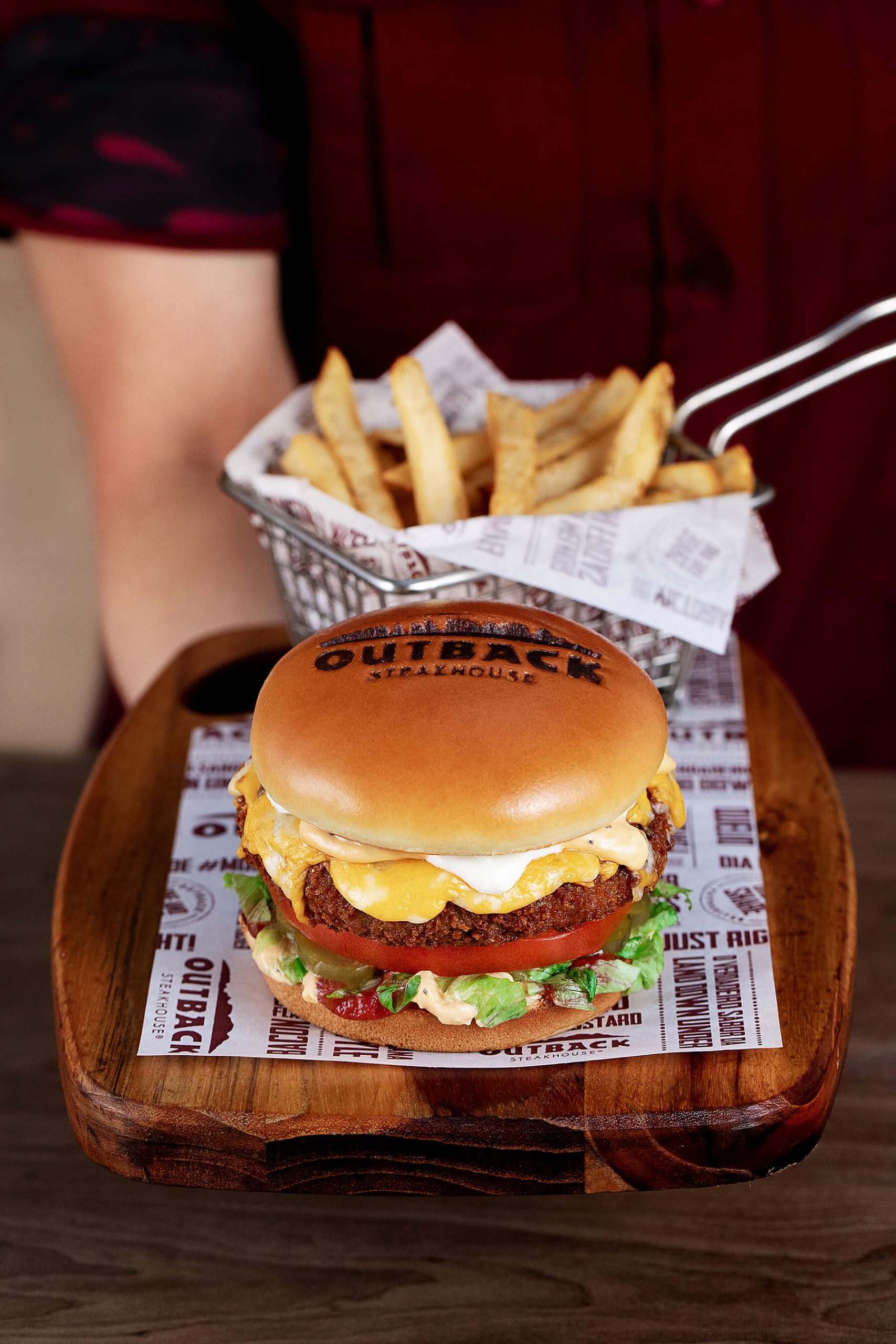 Atendente com uniforme vermelho, servindo um Veggie Burger hambúrguer e batata frita.